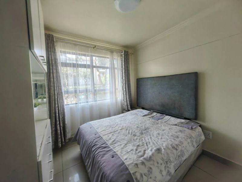 A functional bedroom featuring tiled flooring, built-in cupboards, and a large window allowing natural light.