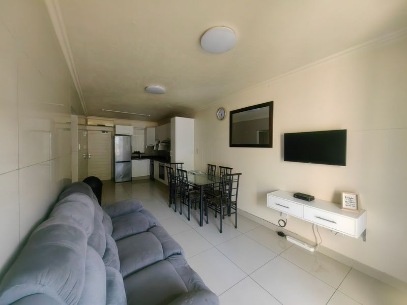 Open-plan living and dining area featuring tiled flooring and a compact kitchen with built-in cabinetry and integrated appliances.