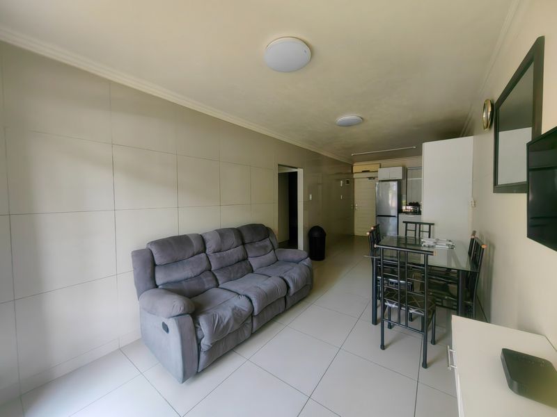 An open-plan living and dining area featuring neutral tiled flooring and flush mount ceiling lights, seamlessly connecting to a compact kitchen space.