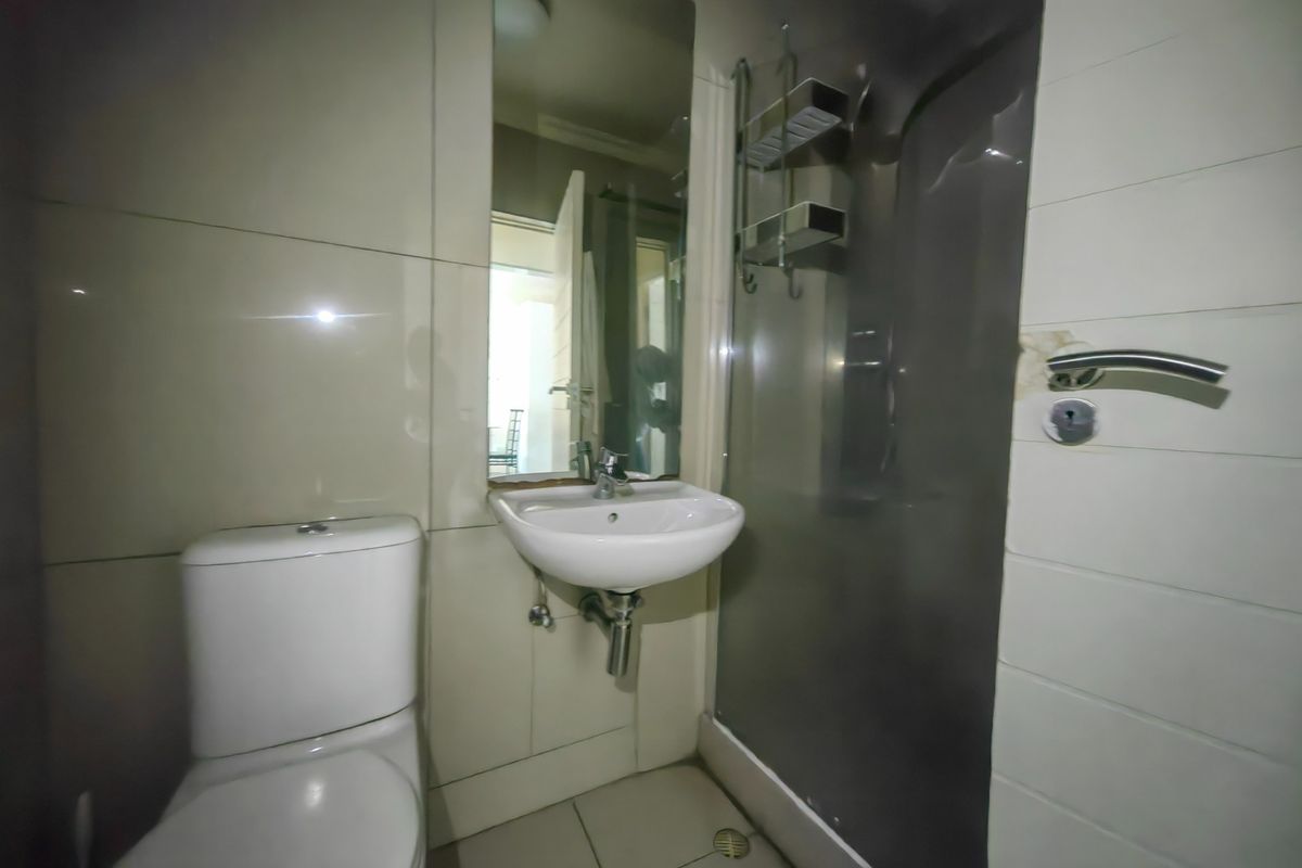 Compact bathroom featuring a wall-mounted basin, toilet, and shower enclosure with tiled finishes. Requires minor repairs to wall and shower fixtures.