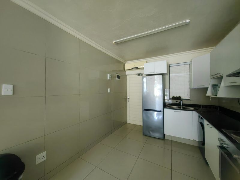 A functional kitchen featuring tiled walls, dark stone countertops, built-in cabinetry, and integrated appliances, including an oven and extractor fan.