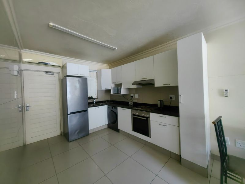 A functional kitchen featuring white cabinetry, dark stone countertops, built-in oven and hob, and tiled flooring, providing a clean and practical cooking space.
