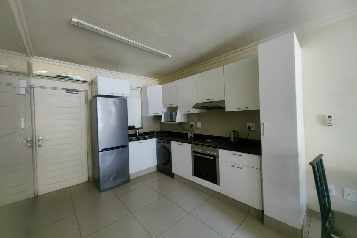 A functional kitchen featuring white cabinetry, dark stone countertops, built-in oven and hob, and tiled flooring, providing a clean and practical cooking space.