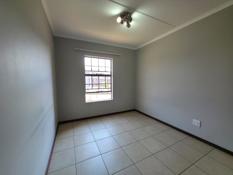 A clean, empty bedroom featuring neutral grey walls, tiled flooring, and a window with security bars, providing a versatile space ready for furnishing.
