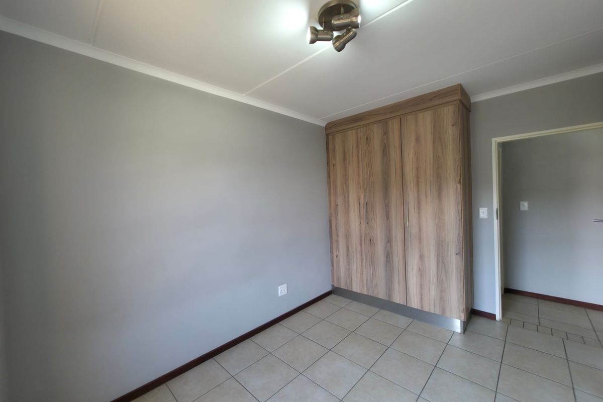 A clean, empty bedroom featuring neutral grey walls, tiled flooring, and a modern wood-finish built-in wardrobe.