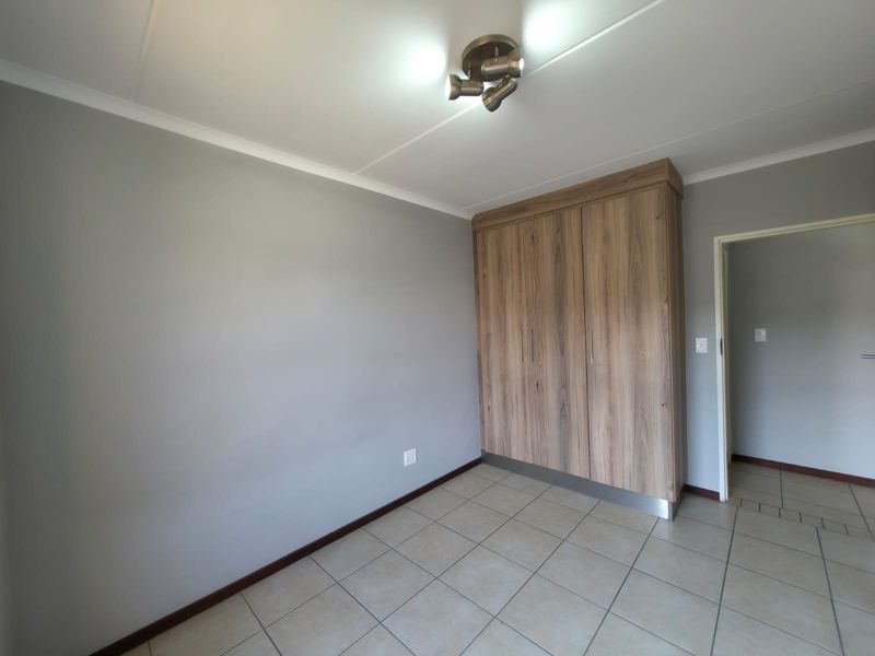 A clean, empty bedroom featuring neutral grey walls, tiled flooring, and a modern wood-finish built-in wardrobe.