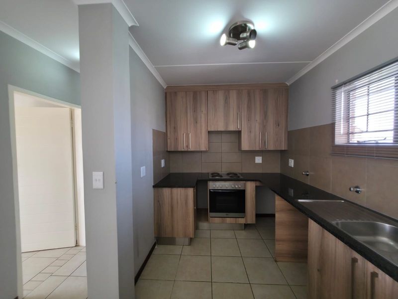 A clean, functional kitchen featuring wood-finish cabinetry, granite countertops, built-in oven and hob, and neutral tiled flooring and splashbacks.