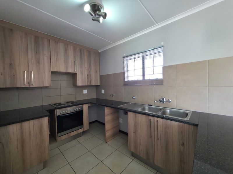 A clean, functional kitchen featuring wood-look cabinetry, granite countertops, a double sink, and a built-in oven with an electric hob.