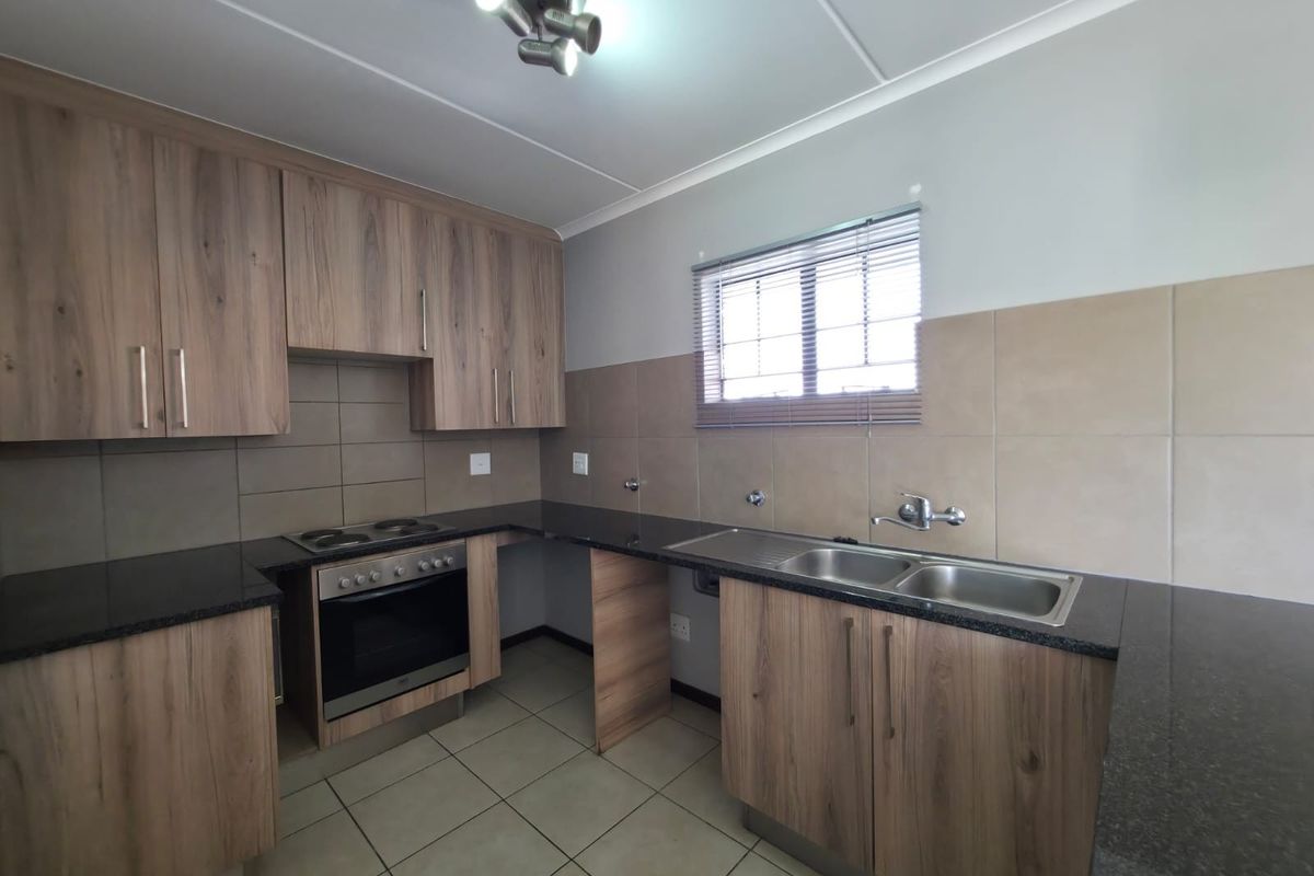 A clean, functional kitchen featuring wood-look cabinetry, granite countertops, a double sink, and a built-in oven with an electric hob.