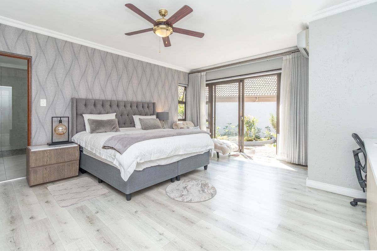Spacious bedroom featuring modern laminate flooring, textured feature wall, ceiling fan, air conditioning, and sliding glass doors leading to a private outdoor area.