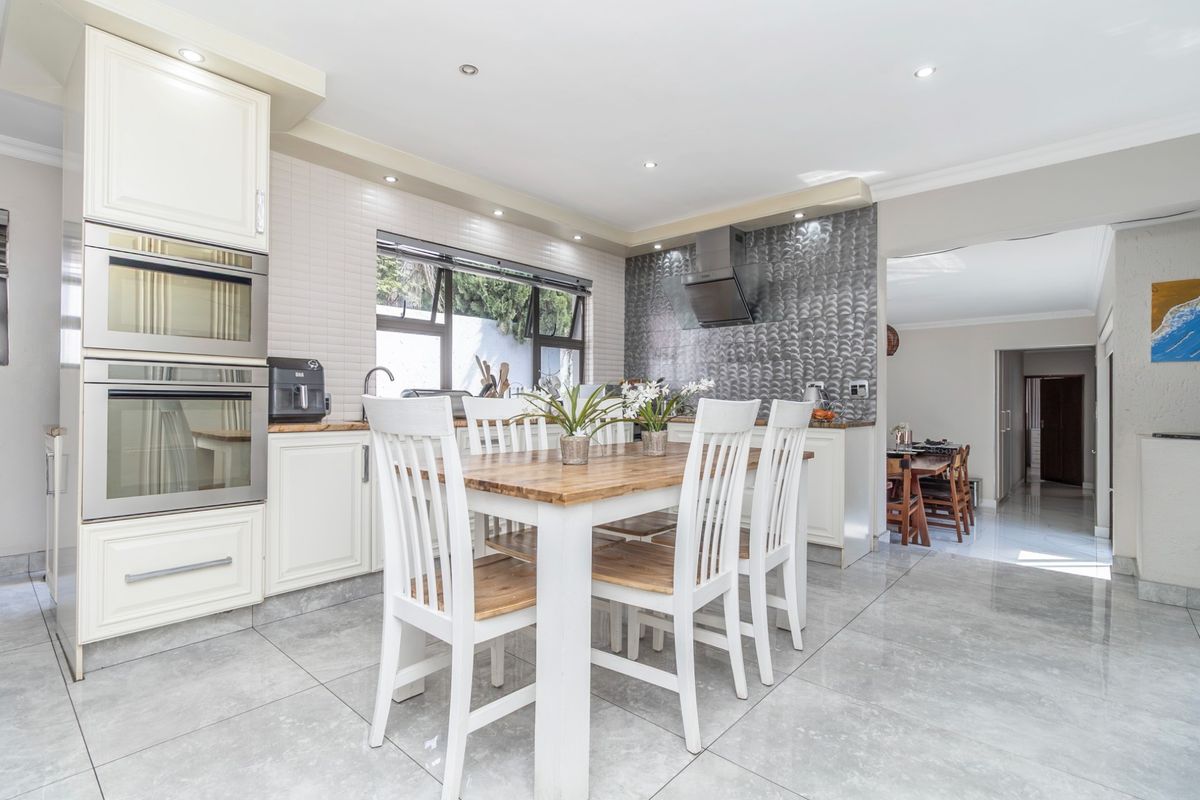 Modern kitchen featuring built-in double ovens, a stylish textured splashback, recessed lighting, and high-quality tiled flooring, seamlessly flowing into the adjacent dining area.