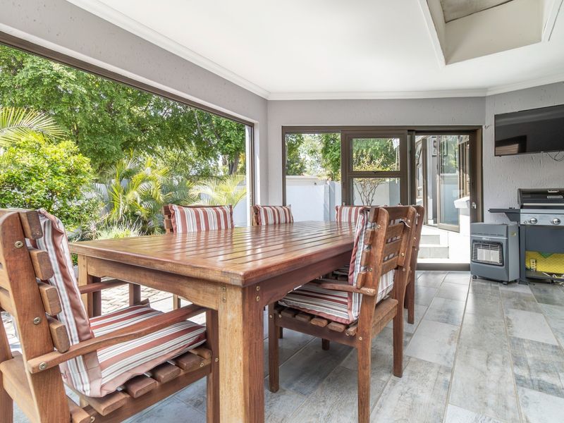A covered patio area featuring tiled flooring, large sliding glass doors, and a wall-mounted television, providing a seamless transition to the garden.