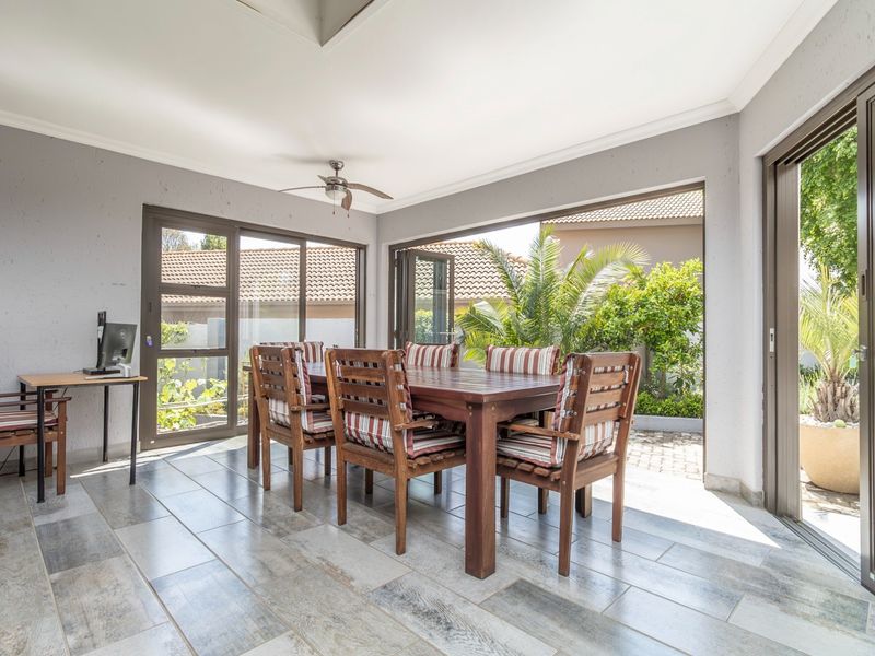 A bright, covered patio area featuring tiled flooring, a ceiling fan, and large sliding glass doors that open to the garden.