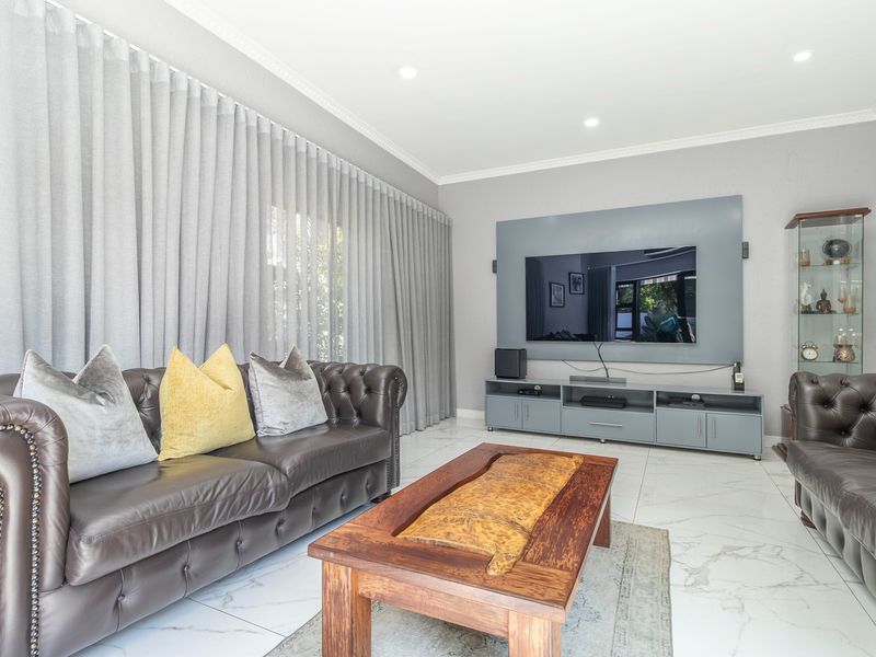 A well-maintained living room featuring marble-look floor tiles, recessed downlights, and a custom built-in media console with integrated wall paneling.