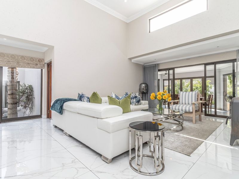 Spacious double-volume living room featuring polished marble-look floor tiles, abundant natural light from large sliding doors, and a modern wood-burning fireplace.