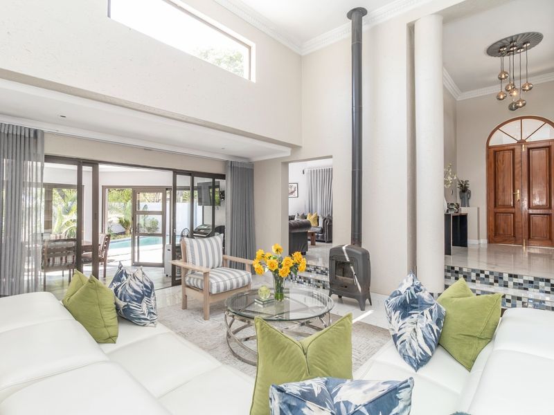Spacious living room featuring a double volume ceiling, a modern freestanding fireplace, and large sliding doors providing seamless access to the outdoor pool area.
