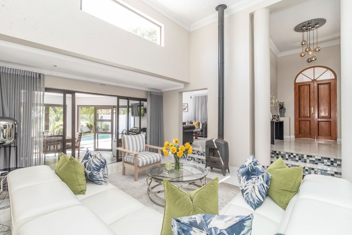 Spacious living room featuring a double volume ceiling, a modern freestanding fireplace, and large sliding doors providing seamless access to the outdoor pool area.