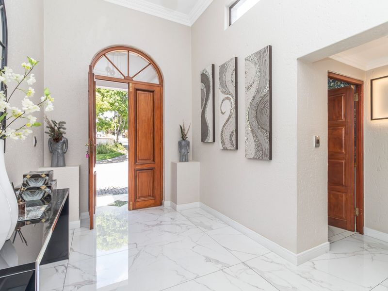 Bright and welcoming entrance hall featuring polished marble-look floor tiles, an elegant arched timber front door, and high ceilings with decorative cornicing.