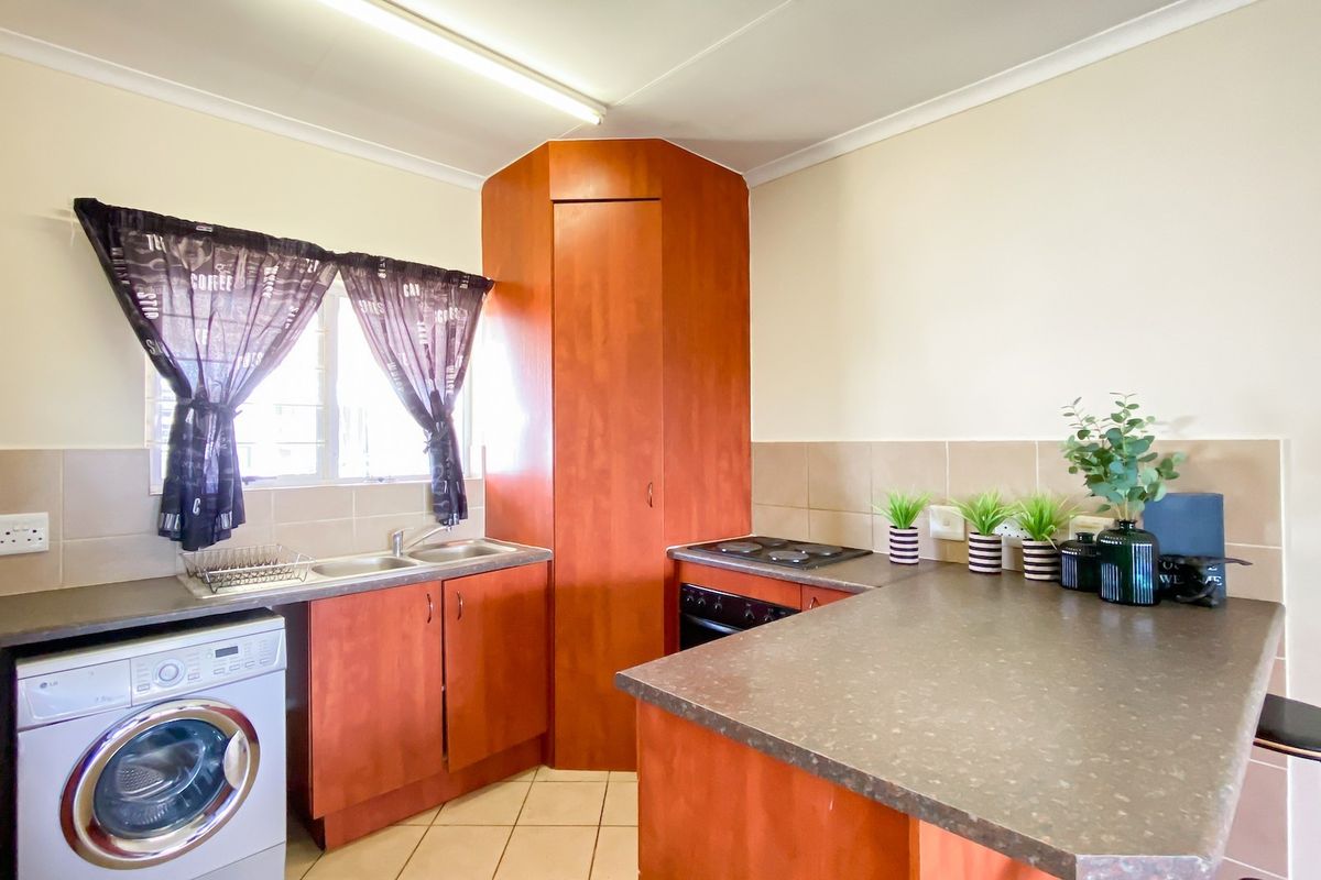 Functional kitchen featuring laminate cabinetry, built-in oven with electric hob, double basin sink, and tiled backsplash with neutral flooring.