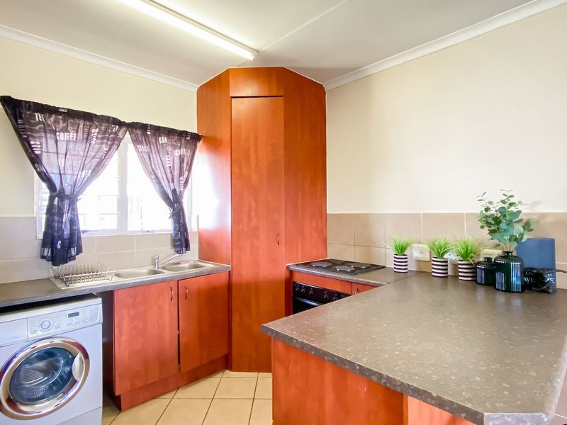Functional kitchen featuring laminate cabinetry, built-in oven with electric hob, double basin sink, and tiled backsplash with neutral flooring.