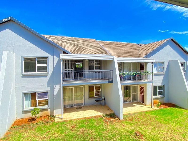 Rear view of a multi-story apartment complex featuring tiled roof, private balconies, ground-floor patios, and sliding glass doors overlooking a shared lawn area.