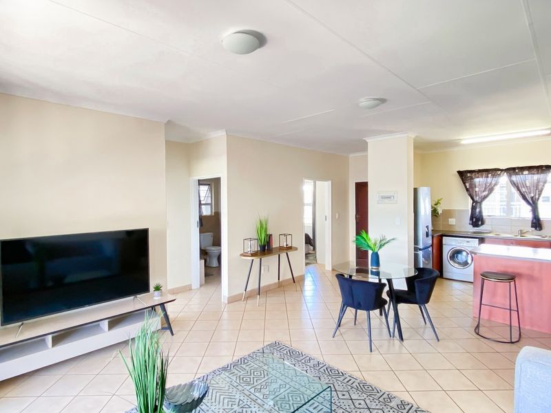 Open-plan living and kitchen area featuring tiled flooring, functional cabinetry, and a breakfast bar, providing a versatile and connected living space.