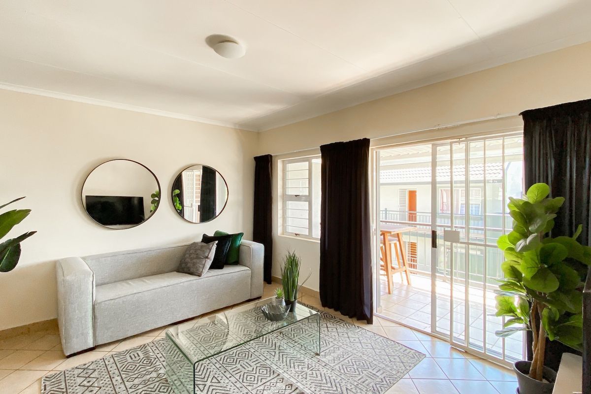 A bright living room featuring tiled flooring and a sliding glass door with a security gate, providing direct access to an outdoor balcony area.