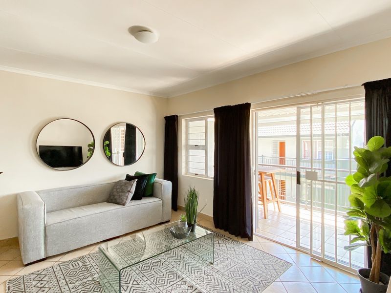 A bright living room featuring tiled flooring and a sliding glass door with a security gate, providing direct access to an outdoor balcony area.