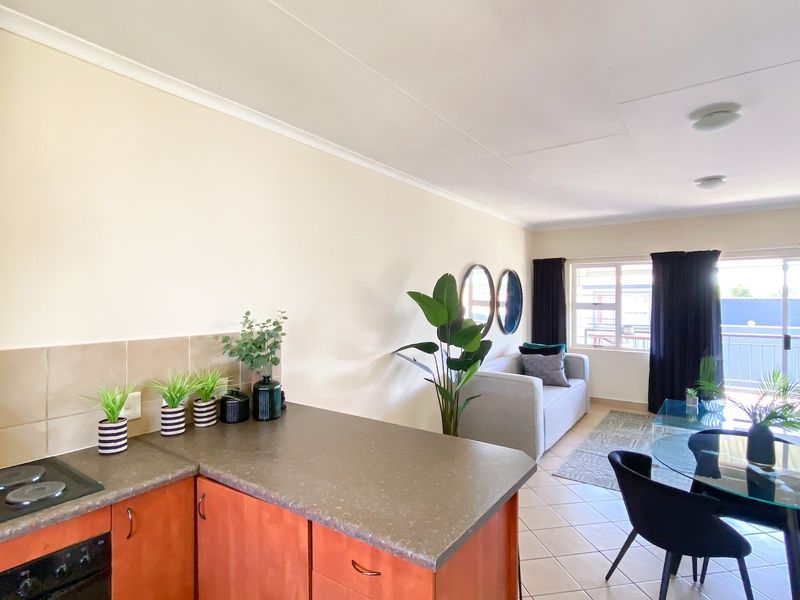 Open-plan living area featuring a functional kitchen with built-in cabinetry, electric hob, and oven, flowing into a bright lounge with access to a balcony.