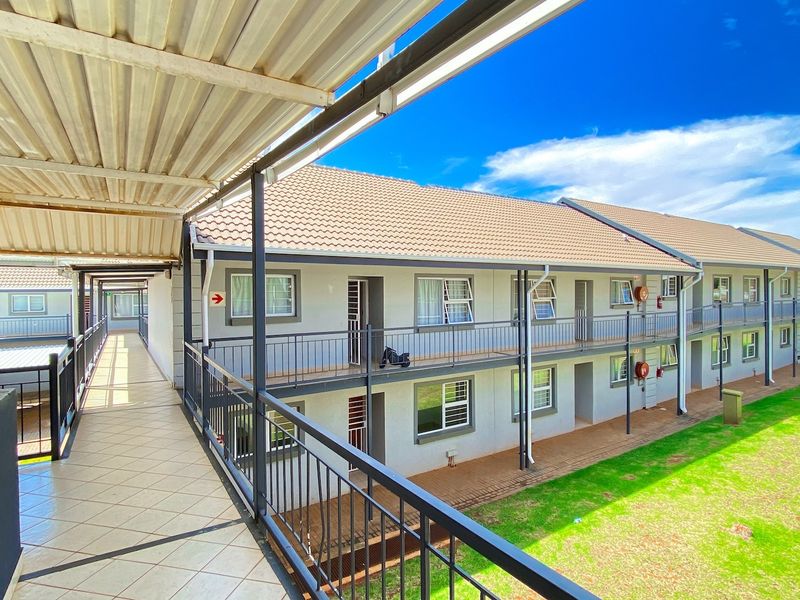 Exterior view of an apartment complex featuring a covered walkway, metal railings, and a well-maintained lawn area.