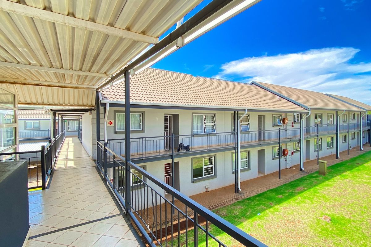 Exterior view of an apartment complex featuring a covered walkway, metal railings, and a well-maintained lawn area.