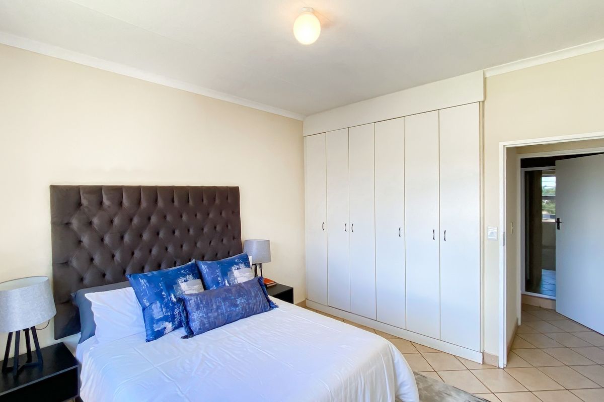 A well-maintained bedroom featuring neutral walls, tiled flooring, and extensive built-in cupboard storage with a clean, functional layout.