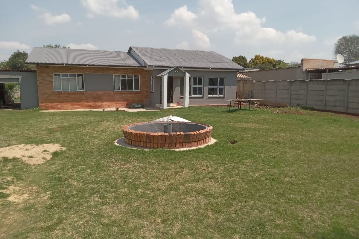 Rear view of a single-story house featuring a large lawn, a circular brick water feature, and a secure precast concrete boundary wall.