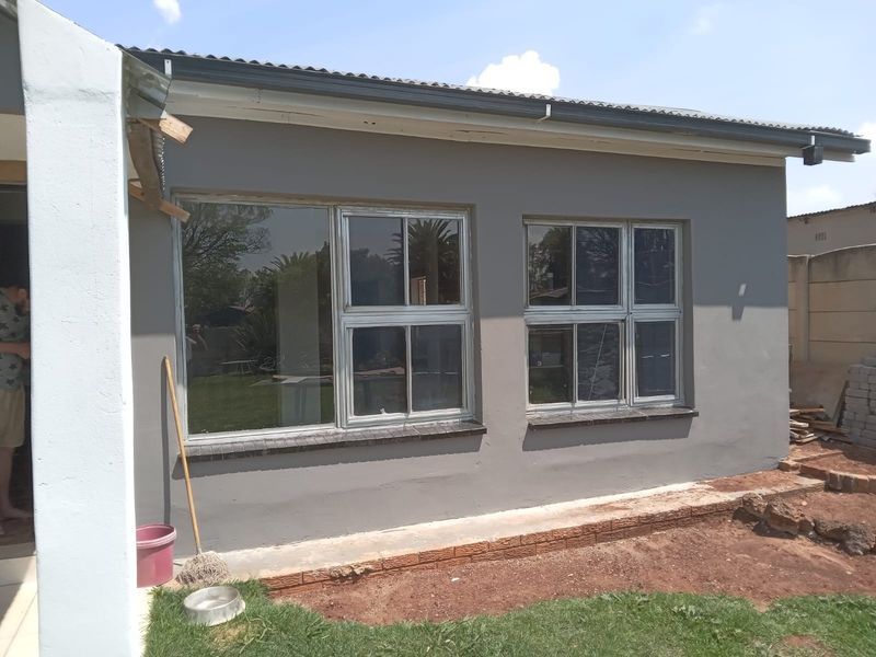Rear exterior view of the house featuring grey painted walls, aluminium window frames, and unfinished landscaping at the base.