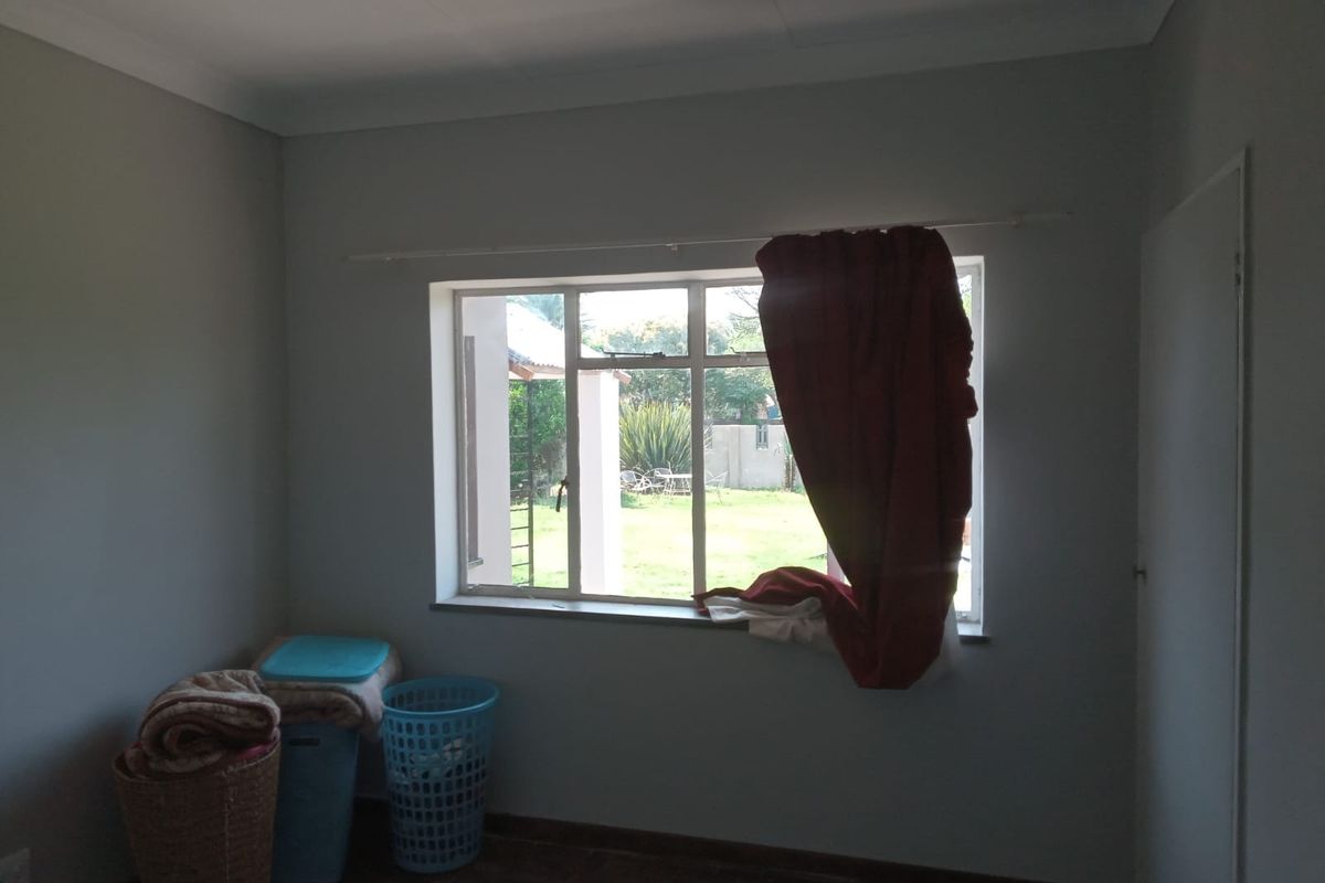 A simple, empty bedroom featuring a steel-framed window with views of the garden and neutral wall finishes.