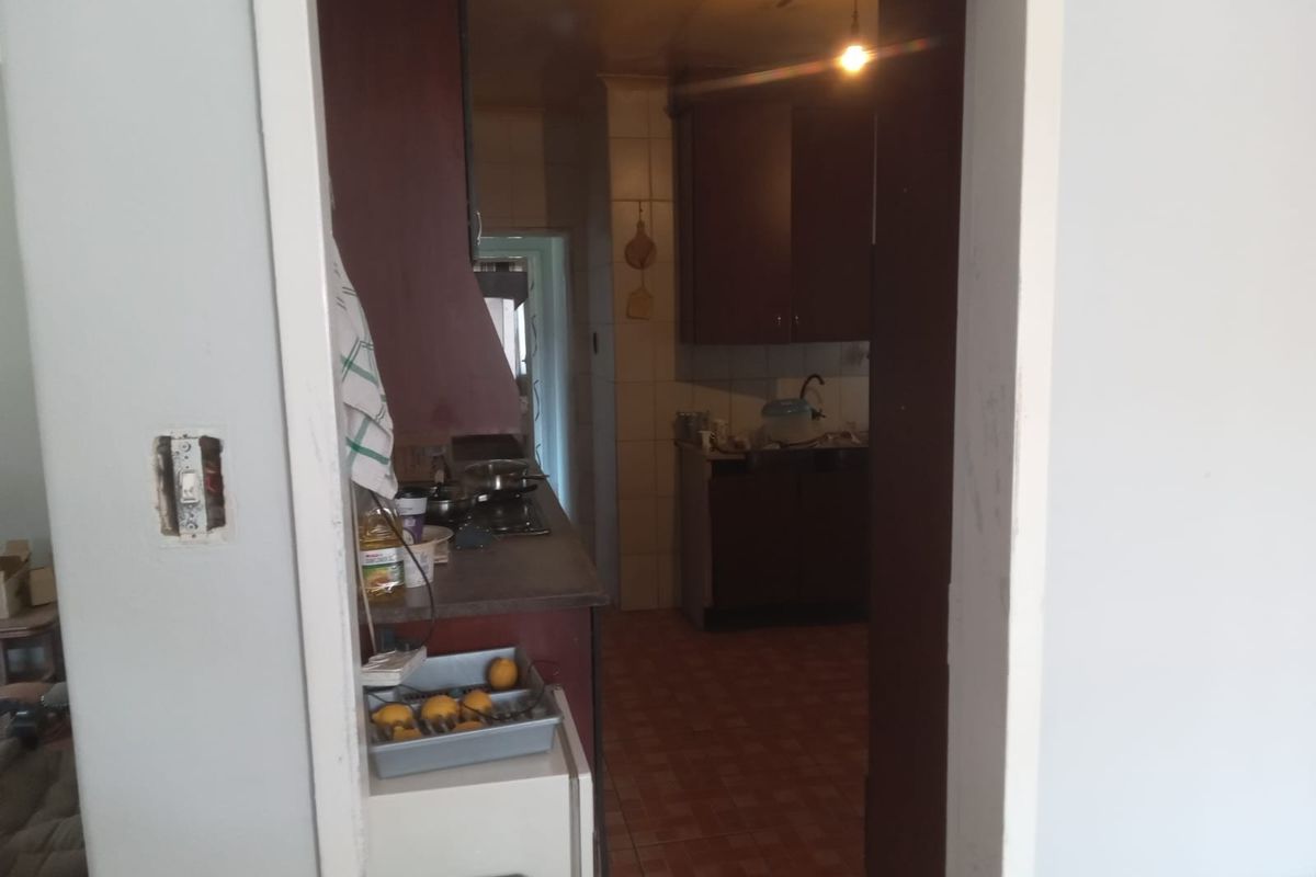 A dated kitchen featuring dark built-in cabinetry, tiled flooring, and a functional hob, viewed through a doorway from an adjacent room.