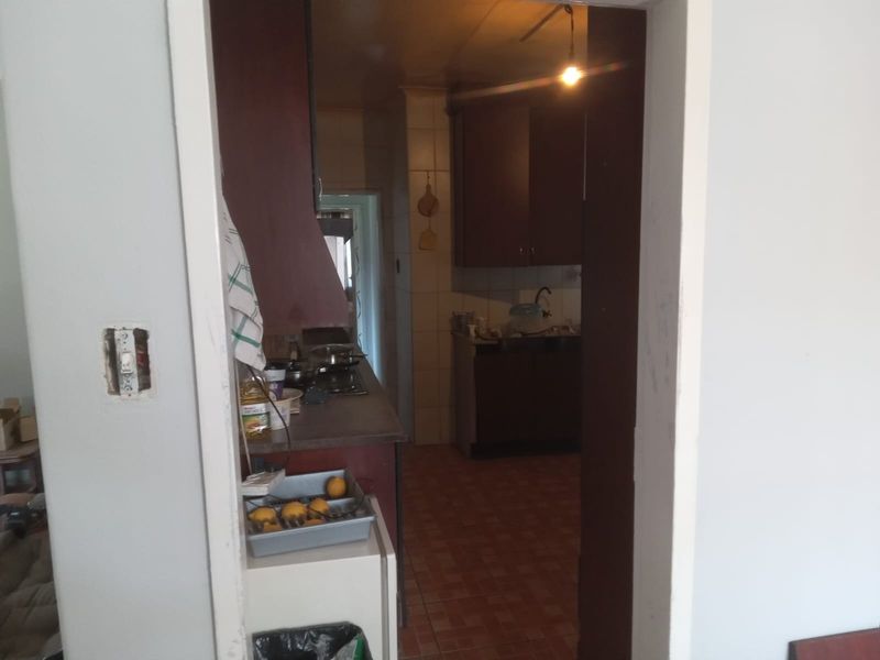 A dated kitchen featuring dark built-in cabinetry, tiled flooring, and a functional hob, viewed through a doorway from an adjacent room.