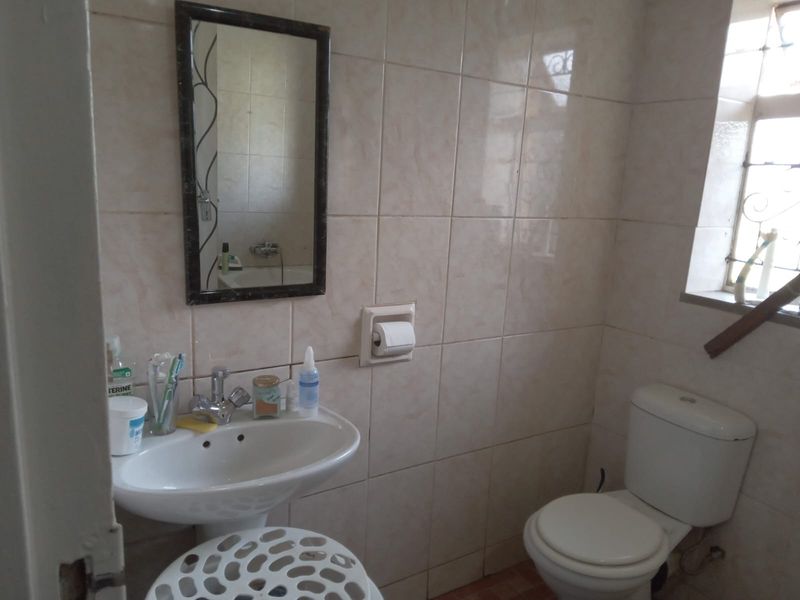 A functional bathroom featuring a pedestal washbasin, toilet, and full-height wall tiling, requiring some cosmetic updates to modernize the space.