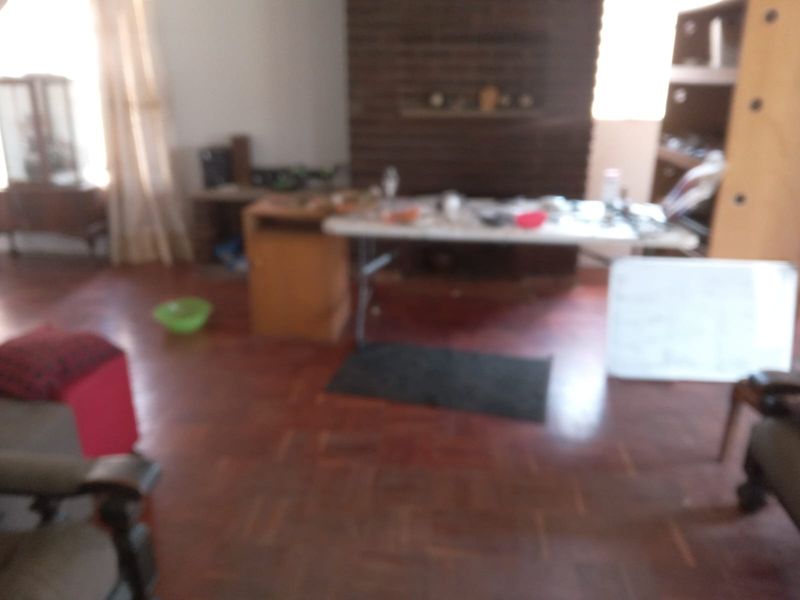 A living room featuring traditional parquet flooring and a brick fireplace, currently used as a multi-purpose living space.