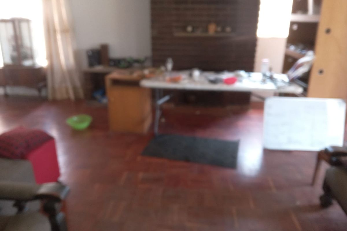 A living room featuring traditional parquet flooring and a brick fireplace, currently used as a multi-purpose living space.