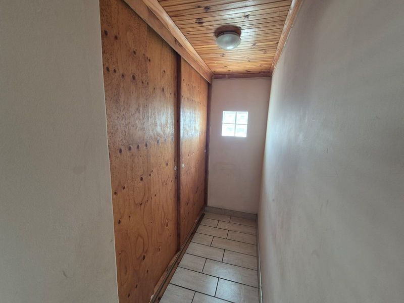 A narrow hallway featuring built-in wooden sliding cupboards, tiled flooring, and a timber-clad ceiling with a small glass block window.
