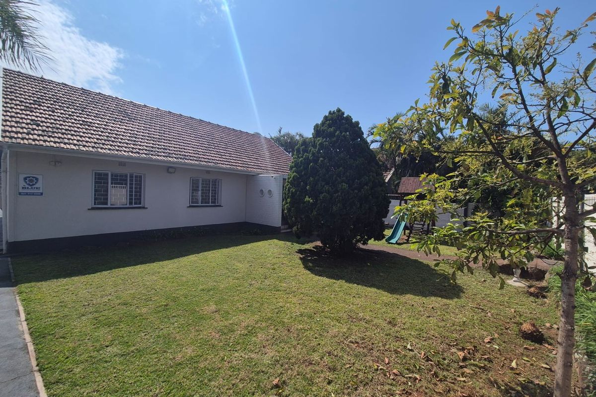 A view of the rear exterior of the house featuring a well-maintained lawn, tiled roof, and security-fitted windows.