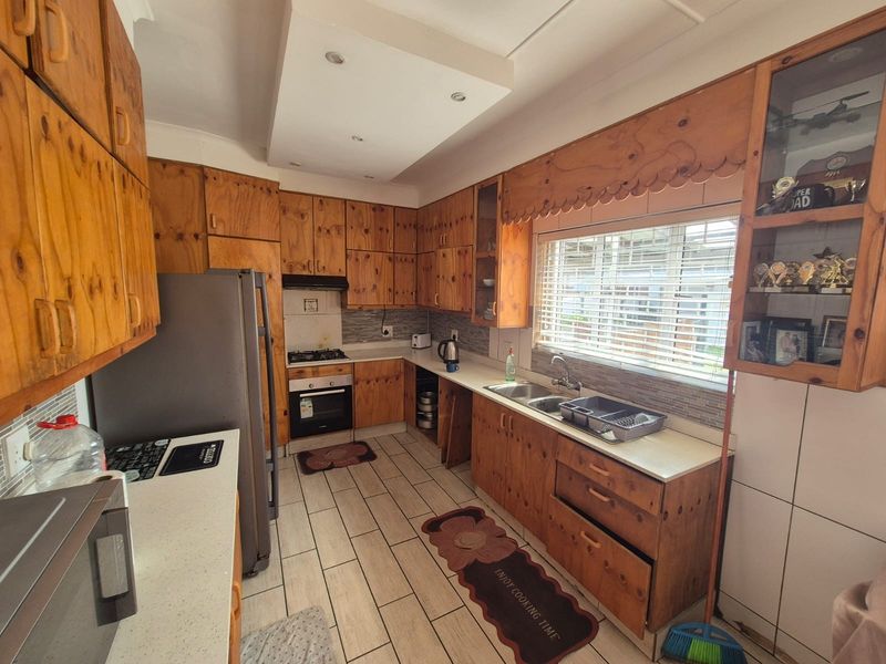 A functional kitchen featuring extensive wooden cabinetry, built-in oven with gas hob, double bowl sink, and tiled flooring throughout.