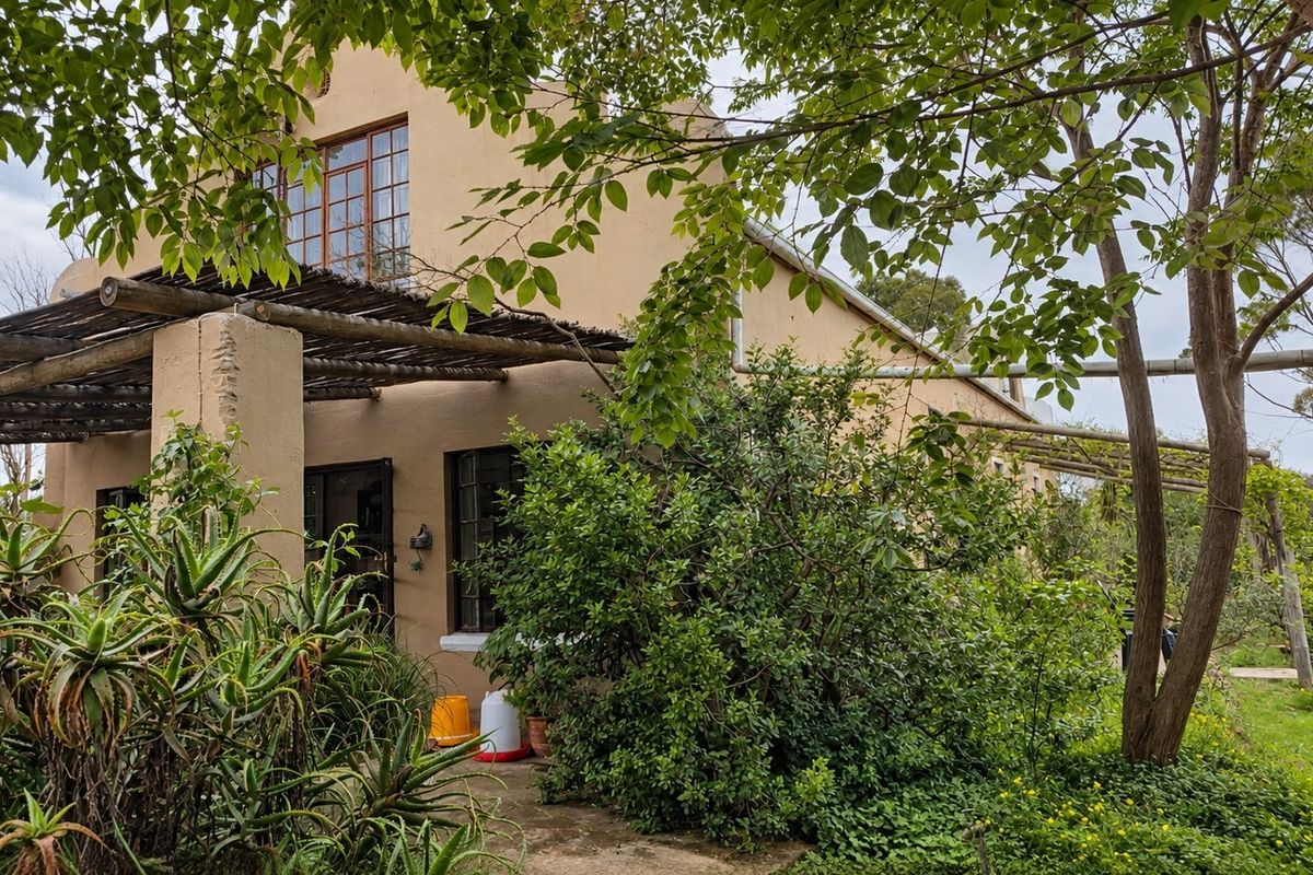 Rear view of the small holding dwelling featuring a timber pergola, established garden, and exterior water storage tank.