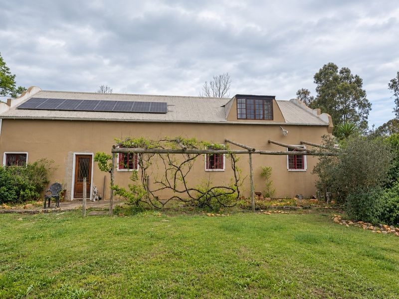 Rear view of a rustic small holding dwelling featuring a corrugated roof with solar panels, a timber pergola, and established garden surroundings.