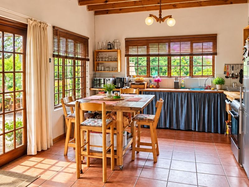 Open-plan kitchen and dining area featuring exposed timber beams, terracotta flooring, and direct access to a patio through timber-framed glass sliding doors.