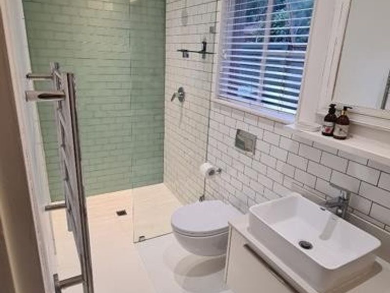 Modern bathroom featuring a floating vanity, wall-mounted toilet, glass shower enclosure with green subway tile accent, and a heated towel rail.