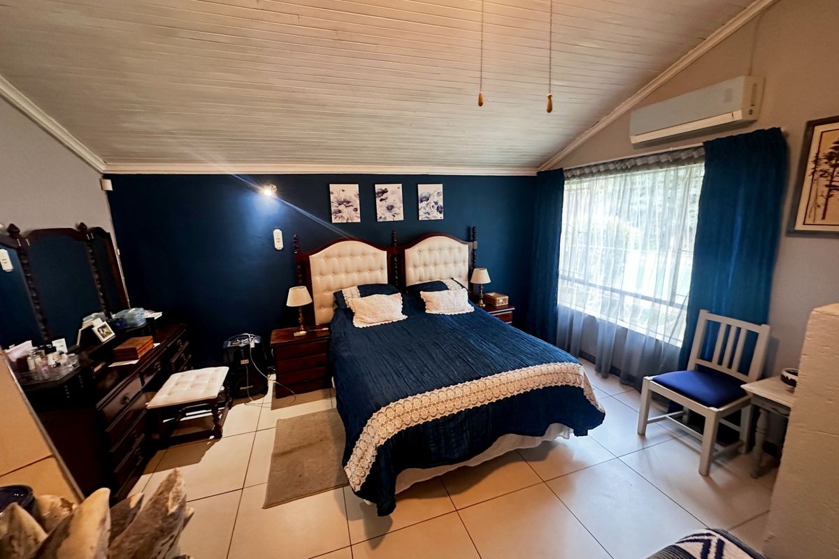 A spacious bedroom featuring tiled flooring, a timber panelled ceiling, and a wall-mounted air conditioning unit.