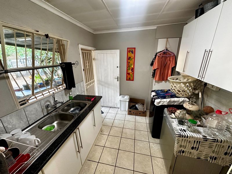 Functional scullery area featuring double bowl sink, laminate countertops, ample built-in cabinetry, and tiled flooring with direct access to the exterior.