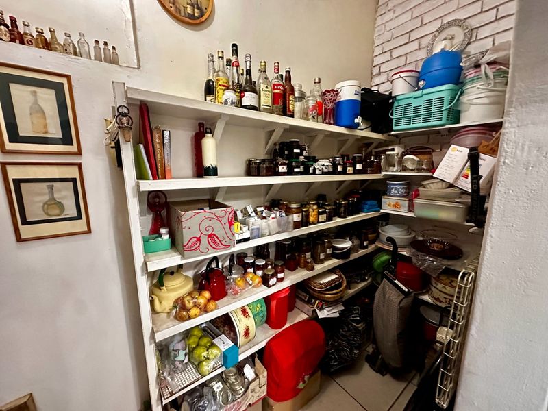 A functional scullery or pantry area featuring extensive built-in shelving and an exposed brick wall finish, providing ample storage space.